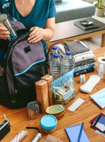 Woman putting cans of food to prepare emergency backpack